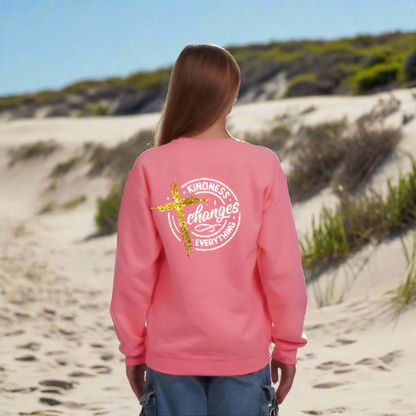 Person wearing a pink sweatshirt with a cross and 'Kindness Changes Everything' text on the back.